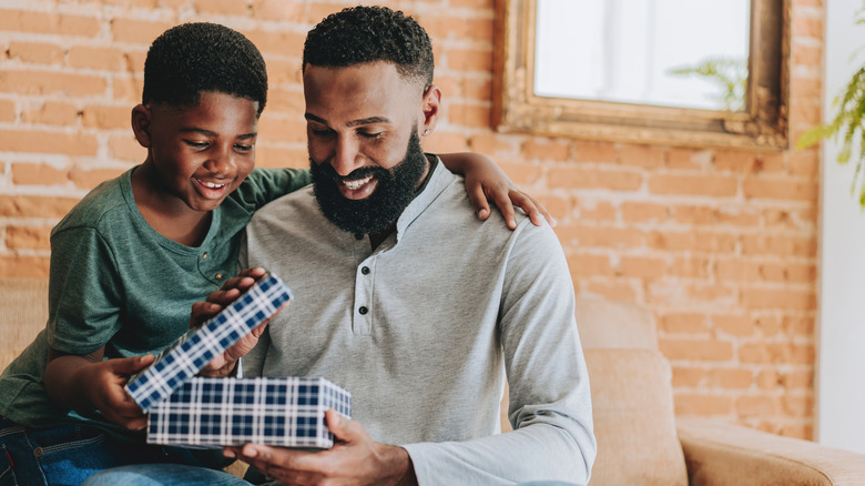 A man opening a gift box with a younger kid beside him