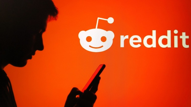 Profile silhouette of a man looking at a phone with Reddit's logo as the background