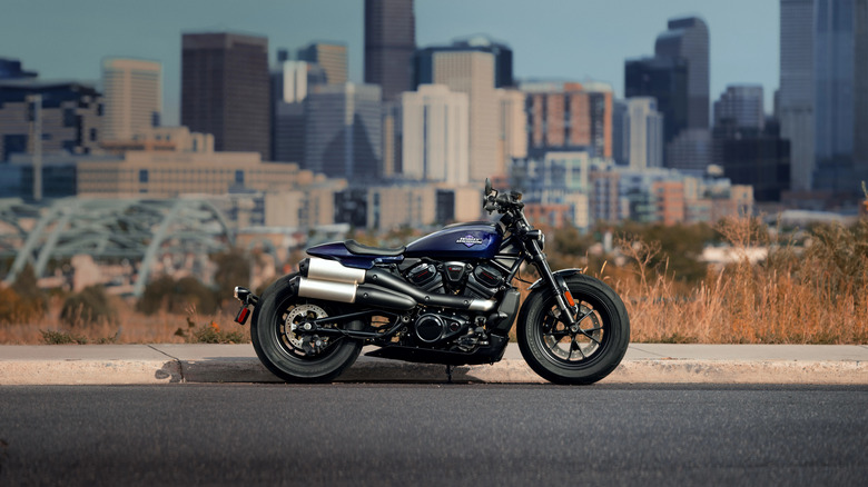 A dark-colored harley-Davidson Sportster S parked in front of a vibrant city skyline