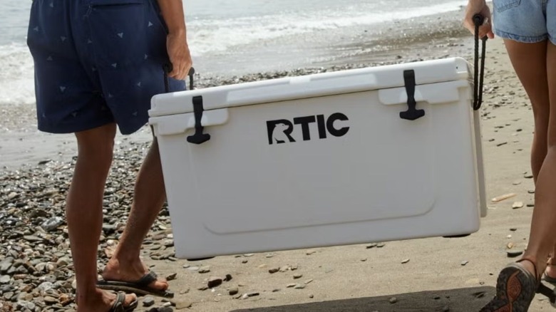 two people carrying rtic cooler on a beach
