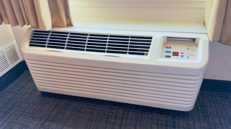A standard white packaged terminal air conditioner (PTAC) installed under a window.