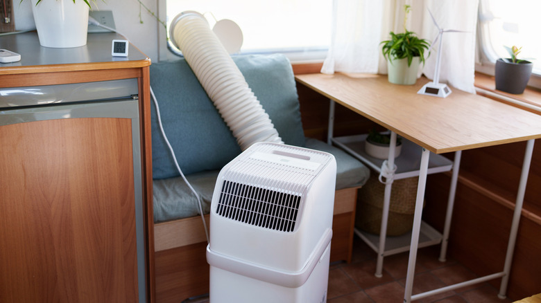 A white portable air conditioner with an exhaust hose installed through a window in a compact room.