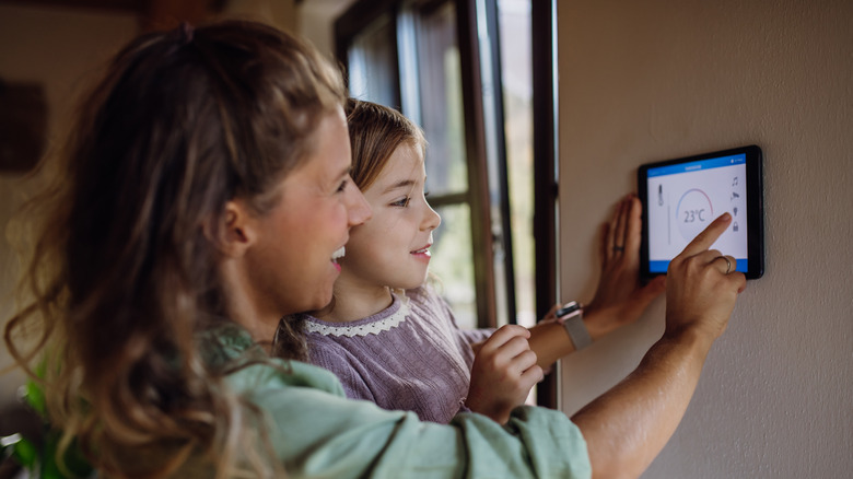 Woman holding young girl while adjusting a thermostat screen