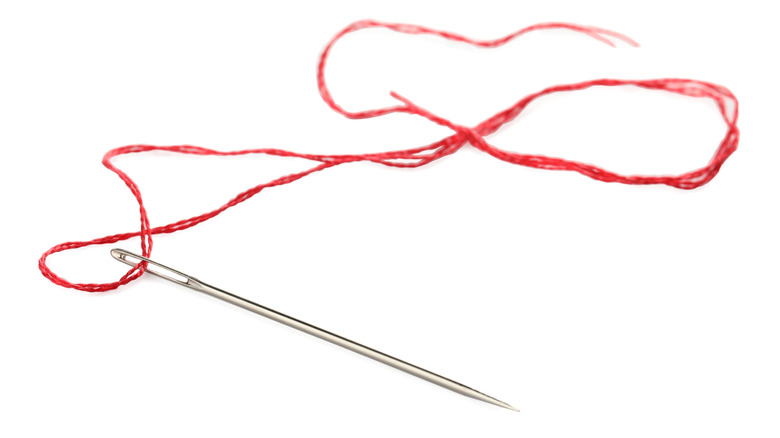 A silver needle with a red thread on a white background