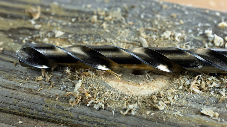 A drill bit sitting on a piece of wood with wood splinters around it