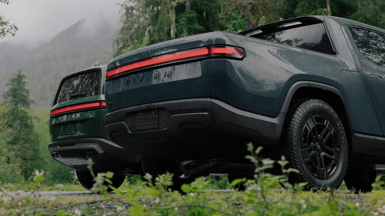 Two Rivian electric vehicles parked outside near a misty forest.