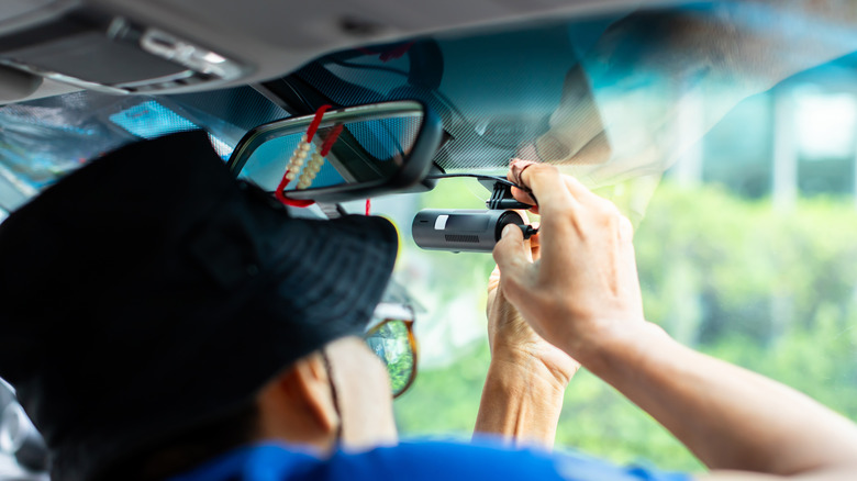 A person in a black bucket hat installing a small dash cam on their windshield