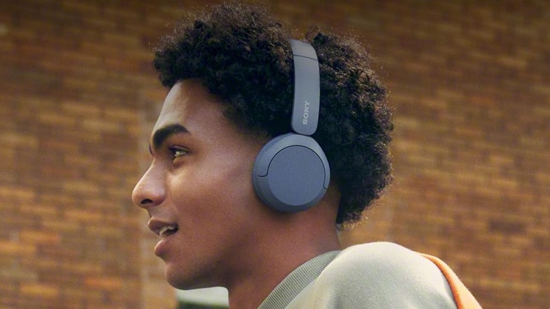 A young African American man wearing blue Sony wireless headphones as he walks past a brick building