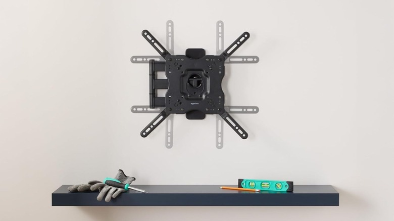 The Amazon Basics Full Motion TV Wall Mount on a wall above a shelf.