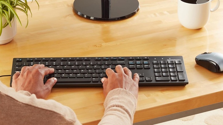 Hands tiping on an Amazon Basics Wired Keyboard on a desk.