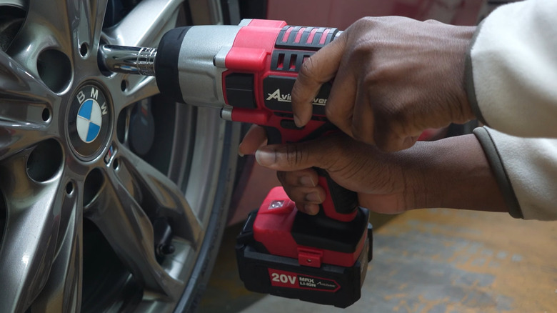 A person using an Avid Power drill with an extension to unbolt a BMW wheel
