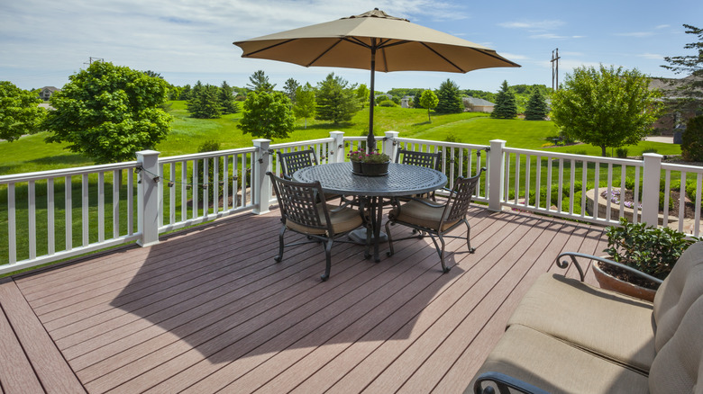 A rural wooden deck with chairs and a sun umbrella on a sunny day