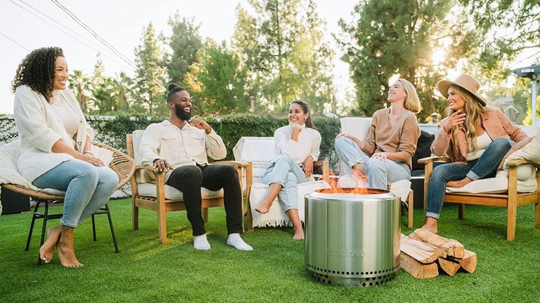 A group of people gathered in a garden, sitting around a Solo Stove smokeless fire pit.