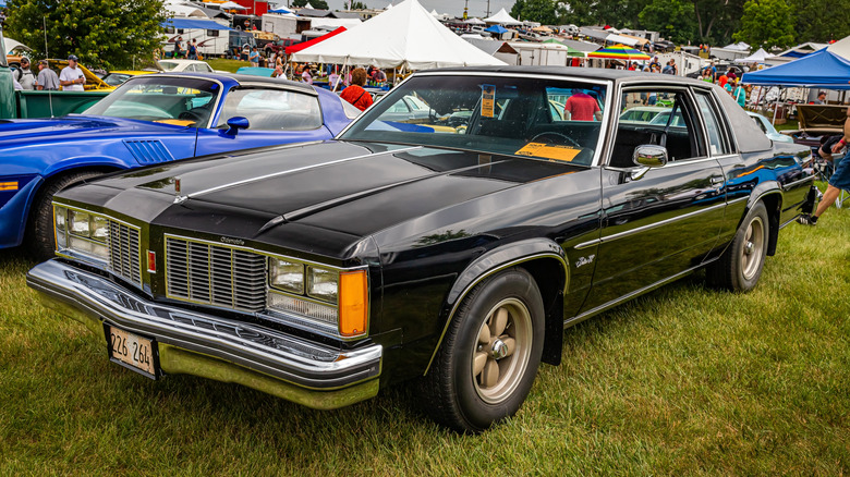 Oldsmobile Delta 88 parked in grass lot at outdoor event