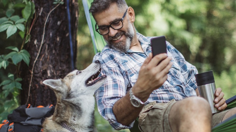Man in hammock with phone and dog sitting next to him