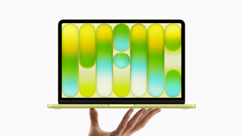 A person holding up a yellow MacBook Neo, studio shot
