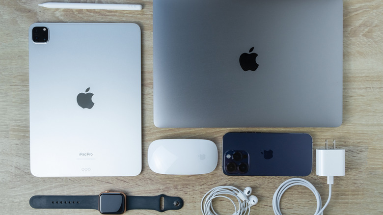 A MacBook, an iPad, an iPhone, an Apple Pencil, a Magic Mouse, an Apple Watch, and a few other Apple devices kept on a wooden table