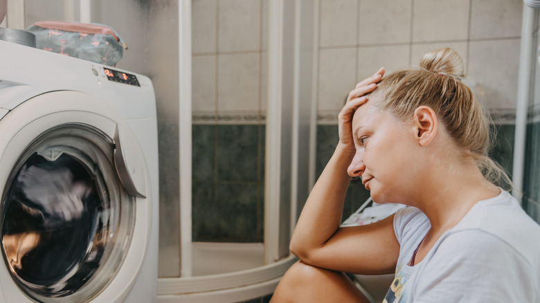 An upset person sitting in front of clothes washing machine.
