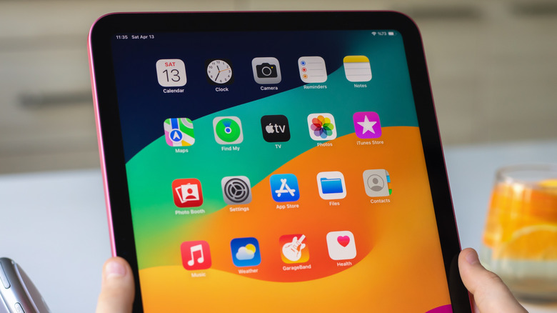 Hands holding an iPad, displaying the home screen with an assortment of app icons.