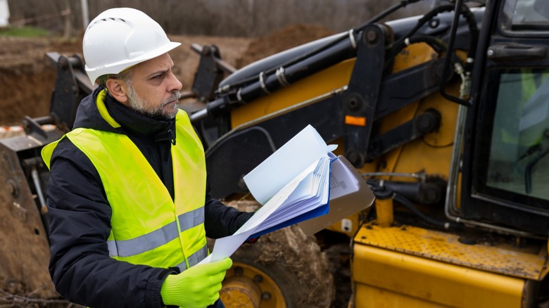Engineer reviews documents beside backhoe loader