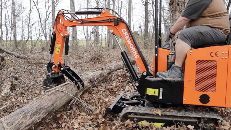 A thumb attachment on a backhoe lifting a log