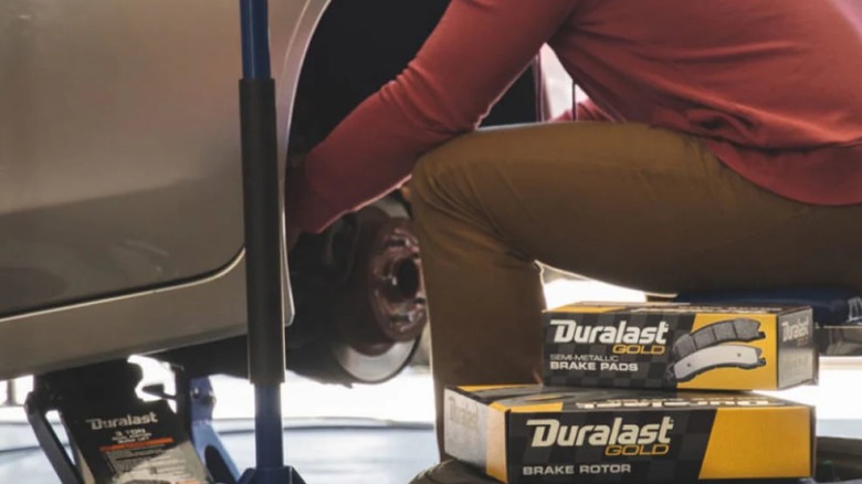 A person performing a brake job with Duralast brake pads and a duralast floor jack