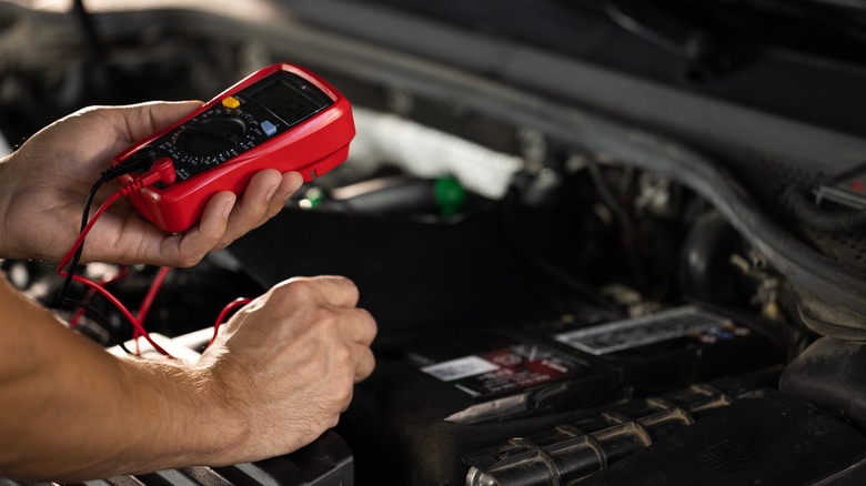 mechanic checking battery with multimeter
