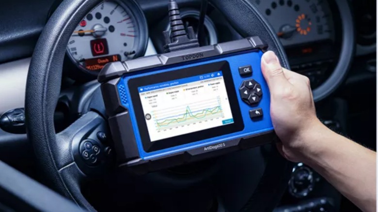 A person using a Topdon OBDII code reader in a car.