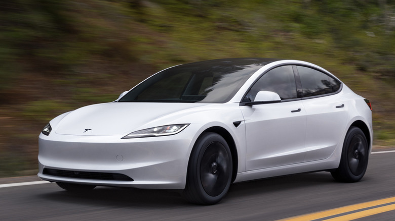 Front 3/4 view of Tesla Model 3 on road in forested area