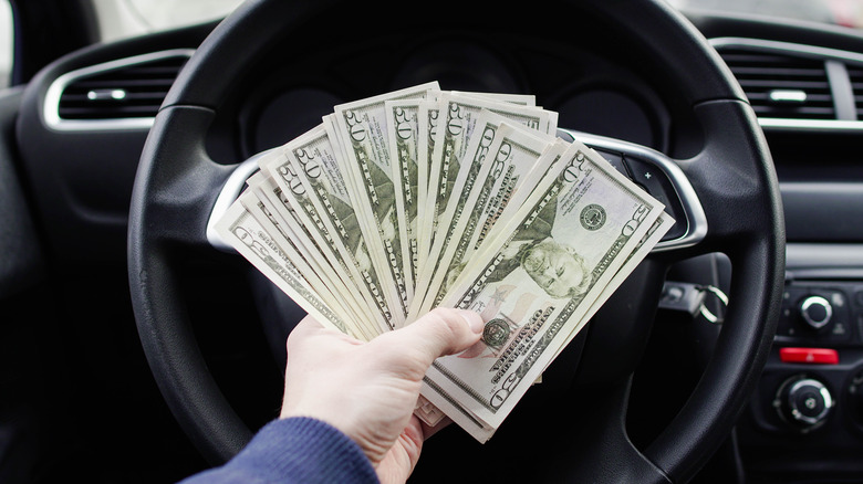 hand holding cash by steering wheel
