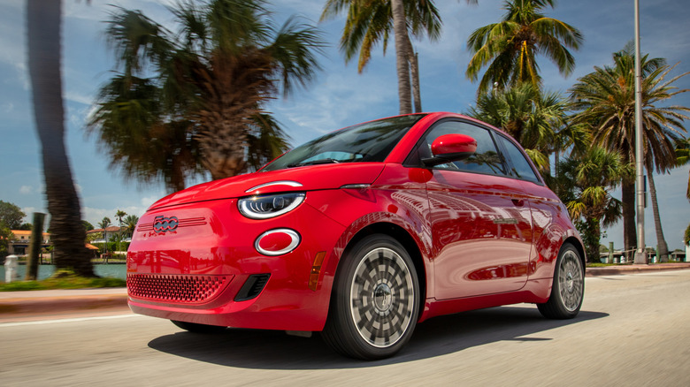 Fiat 500e in red driving on a road with palm trees in the background.