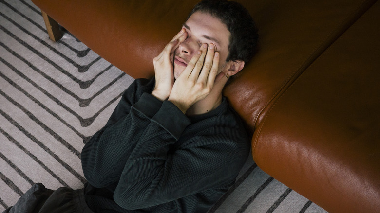 Man on couch rubbing eyes