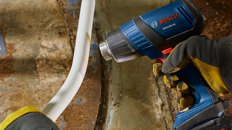 person heating pipes with heat gun