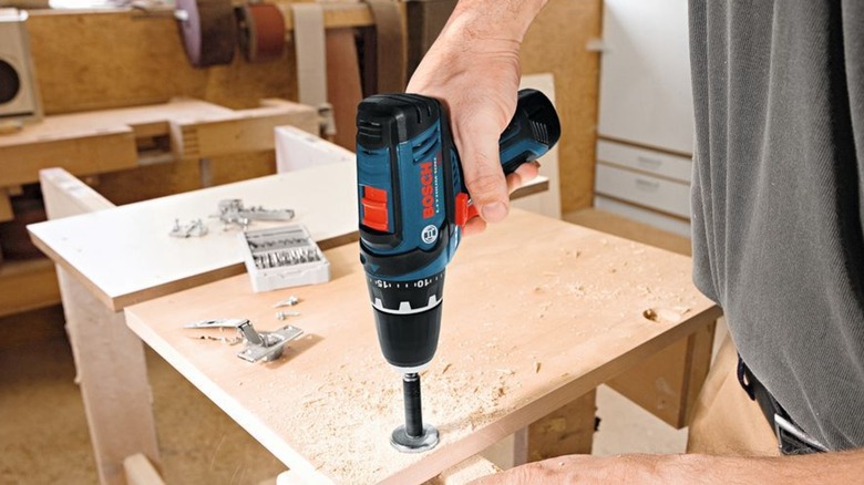 A person using the Bosch 3/8 inch drill/driver in a wooden board.