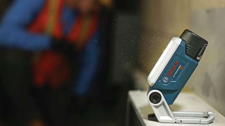 A Bosch LED worklight illuminates a dark room while a worker works.