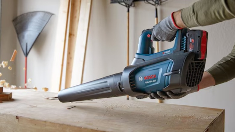A person cleans a garage table with a Bosch blower.