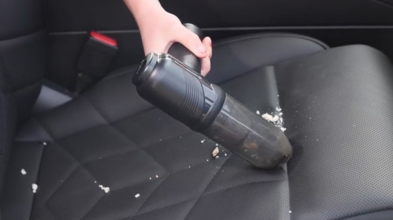 A vehicle seat being cleaned using a hand vacuum