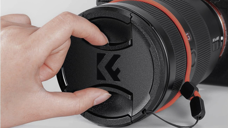 A woman pinching the center of the K&F Concept Professional Lens Cap to remove it.