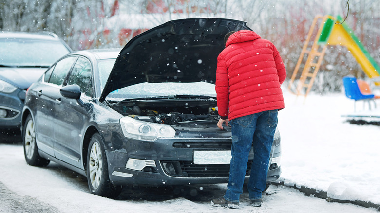 person looking under the hood of a car while it is snowing