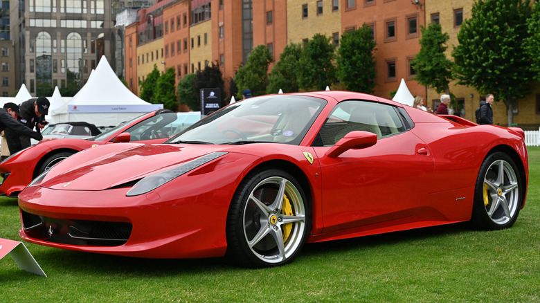 Front 3/4 view of red Ferrari 458 Italia parked on grass at car show.