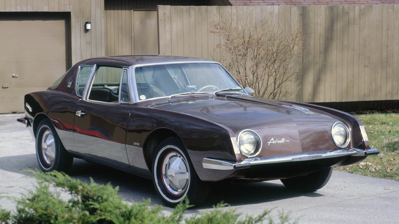 A 1963 Studebaker Avanti, finished here in a metallic gray-brown shade, standing in a driveway in the sun.