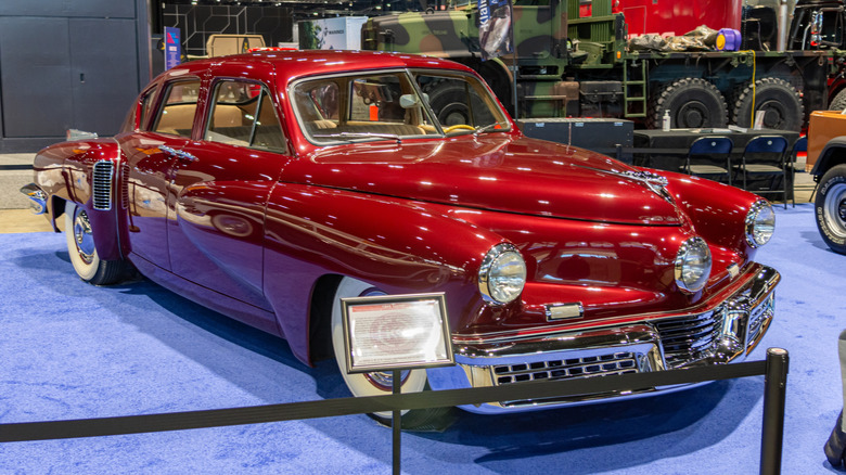 A metallic red Tucker 48 on display behind barriers at an indoor auto show in 2024.