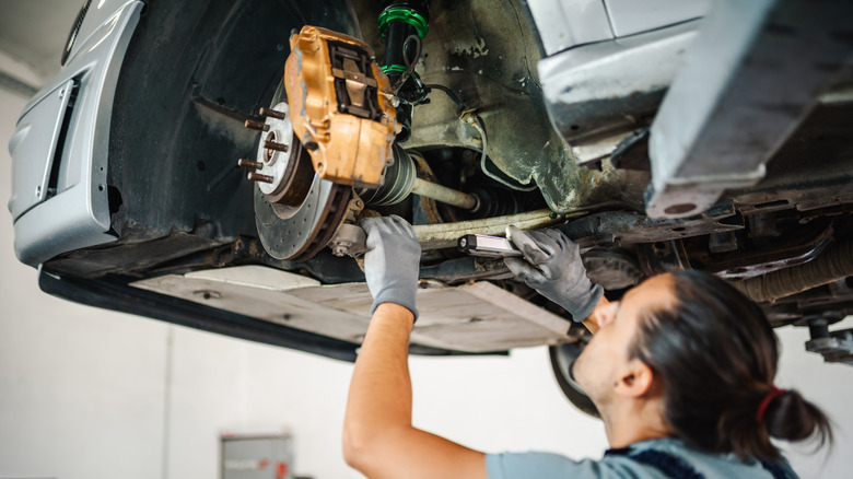 Mechanic inspecting brake and axle on car in auto shop