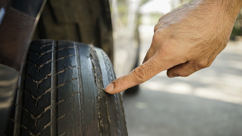 Person pointing to worn-out tread and cracking on a car tire