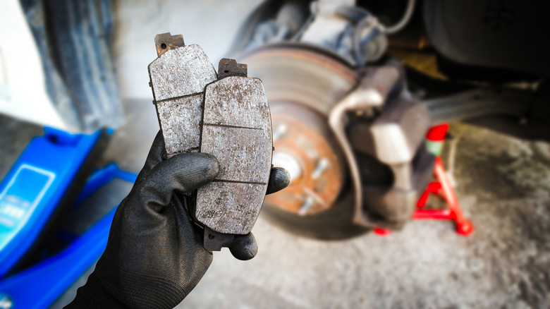 person holding up worn brake pads in front of a rotor