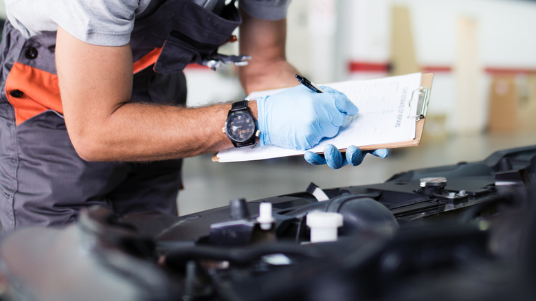 person filling out inspection paperwork over an engine bay