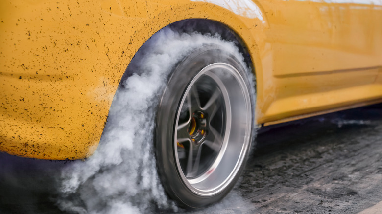 Close-up of a yellow car performing a burnout with smoke emitting from rear tire