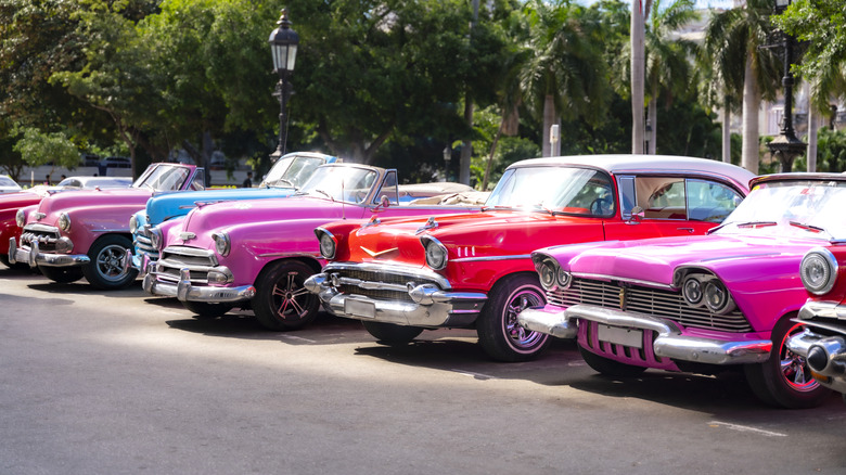 A row of brightly colored American cars parked next to each other in a suburban setting.
