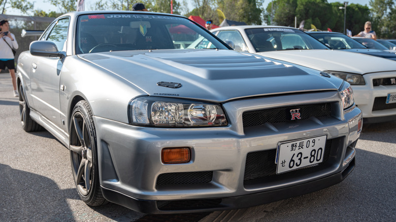 A gray R34 Nissan Skyline parked next to other JDM cars on a JDM car show.
