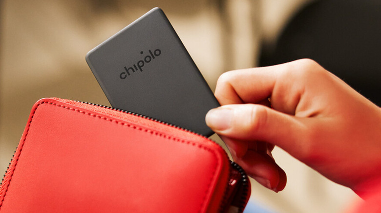 A close up of a hand putting a Chipolo CARD Spot card-shapped wallet tracker into a red wallet with a blurred background